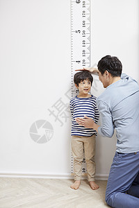 父亲看着墙上的刻度测量孩子身高图片