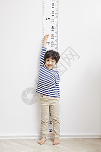 小男孩靠在墙上的刻度测量身高图片