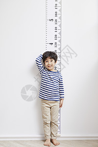 靠在墙上测量身高的小男孩高清图片