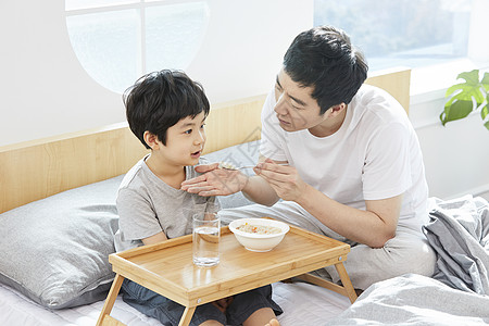 床上喂儿子吃饭的父亲图片素材