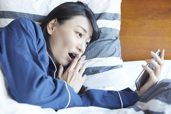 躺在床上看手机开心的女青年图片