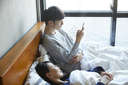 靠在床上看手机的男青年图片