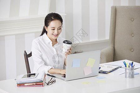 职业女性拿着咖啡看着笔记本电脑图片