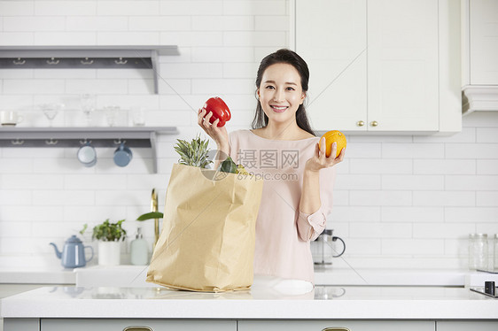 厨房里拿着蔬果微笑的年轻女子图片