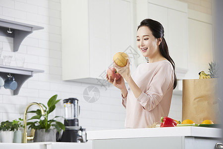 厨房里拿着水果微笑的年轻女子图片