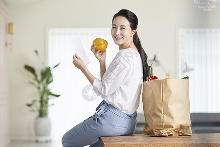 坐在桌上拿着彩椒微笑的女青年图片