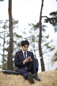 坐在草坪上使用手机的成年男子图片