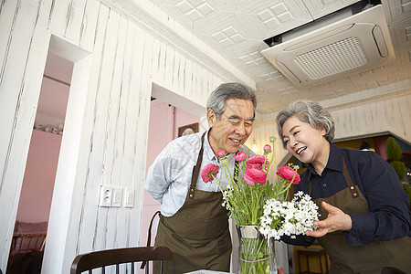 老夫妇戴围裙在室内开心整理花朵图片