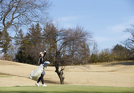 地质队员背着行囊走在女子背着高尔夫球袋走在球场背景
