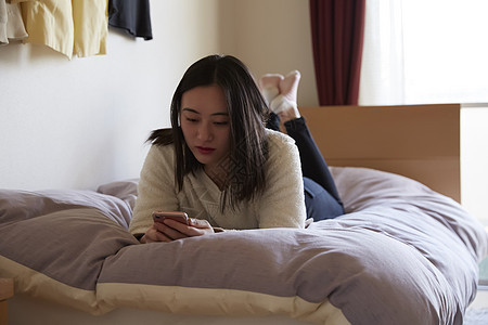 趴在床上玩手机的青年女子图片