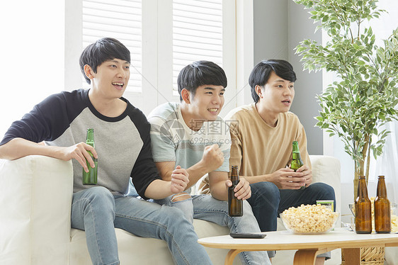 三个好哥们一起在客厅喝啤酒庆祝图片