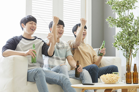 三个好哥们一起在客厅喝啤酒庆祝图片