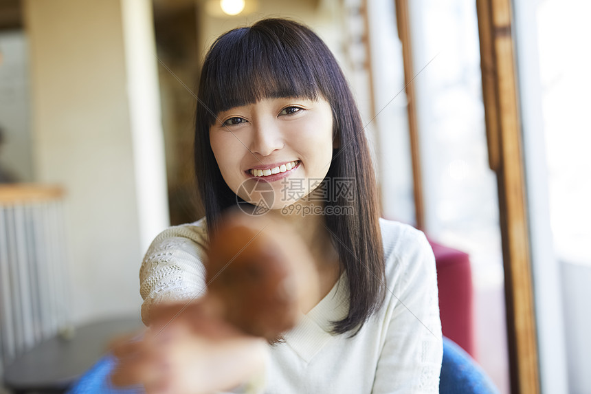 咖啡馆举着面包微笑的年轻女子图片