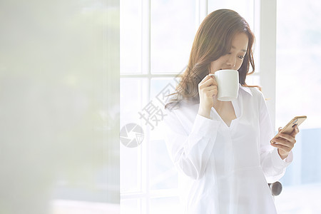 窗边喝咖啡看手机的年轻女子图片