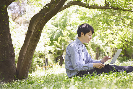 公园草坪上使用电脑的年轻男子图片