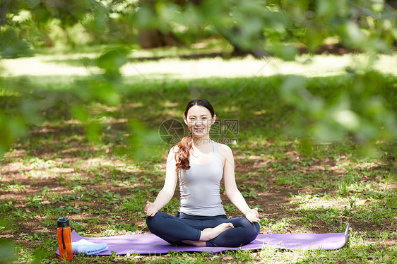公园里坐在瑜伽垫上的青年女子图片