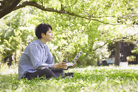 坐在草坪上拿着咖啡的男青年图片