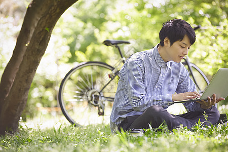 坐在草坪上使用笔记本电脑的男性图片