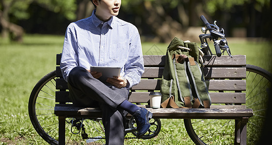 公园长凳上拿着平板电脑的男青年特写图片