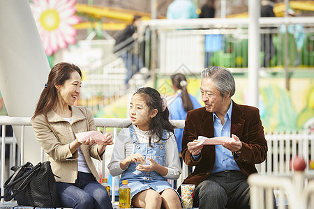 祖父母陪孙女在游乐园里吃小吃图片