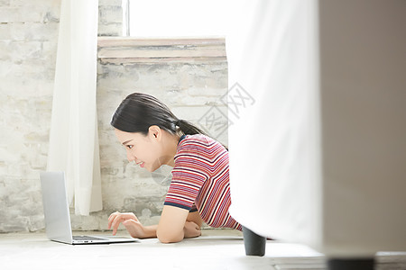 年轻女子趴在地上使用笔记本电脑图片