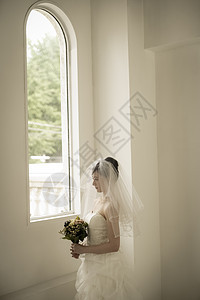 窗边戴着头纱拿着手捧花的新娘图片
