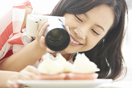 年轻女子微笑的拿相机拍甜品图片