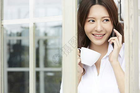 窗口接听电话微笑的年轻女子图片