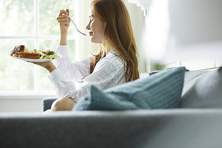 沙发上吃着早餐的年轻女子图片