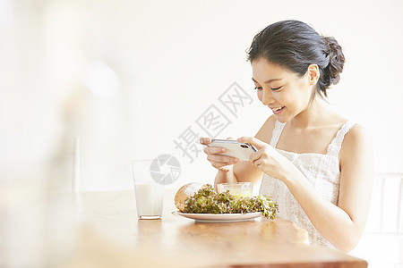 拿着手机拍食物照片的年轻女子图片