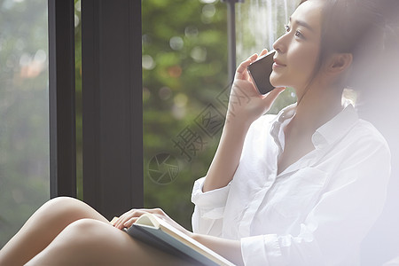 坐在窗边打电话的年轻居家女性图片