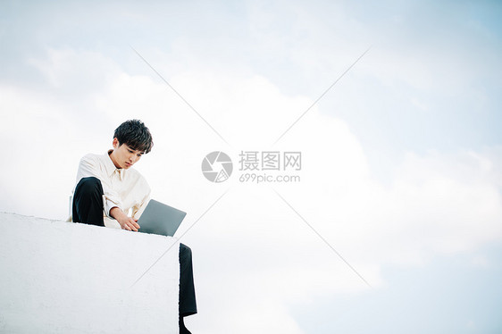 一个男人坐在屋顶上打开一台笔记本电脑图片
