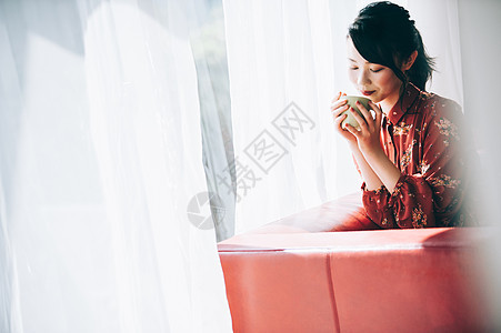 穿着红裙的女孩坐在靠窗的沙发上喝咖啡图片