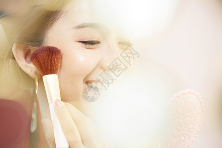 化妆刷轻扫脸颊微笑的年轻女子图片