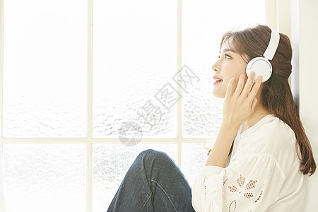 窗边戴着耳机听音乐的年轻女子图片