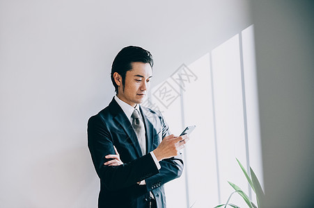 男子套装营销站立对白色墙壁的上司男当看手机时图片