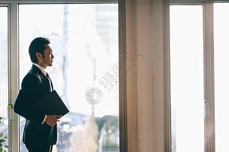 正式青春职业站立与文件的上司人在窗口旁边图片