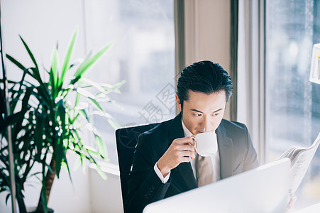 信托处长40多岁读一张报纸的上司人在个人计算机在窗口的一个位子图片