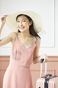 戴着草帽拖着行李箱的度假女性图片