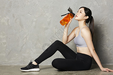 坐在地上喝水休息的运动女性图片