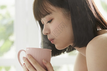 茶杯中的女孩女青年低头将水杯中的水吹凉背景