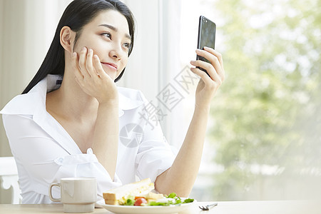 早餐看着手机的年轻女子图片