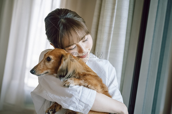 窗边抱着宠物狗的女人图片