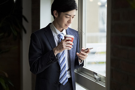 窗户旁喝咖啡看手机的男子图片