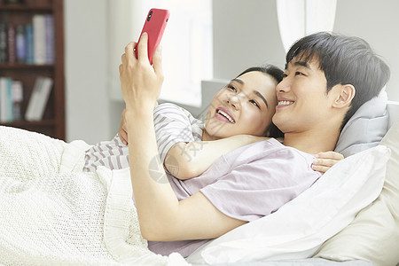 卧室里生活的开心年轻夫妇看手机图片
