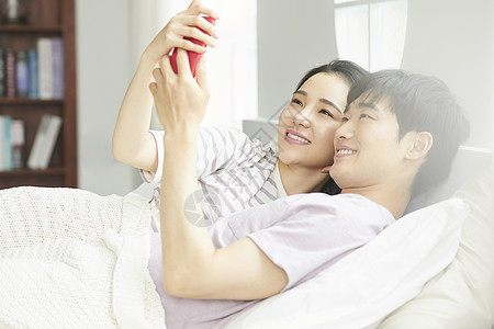年轻夫妻紧密拥抱躺在一起看手机图片