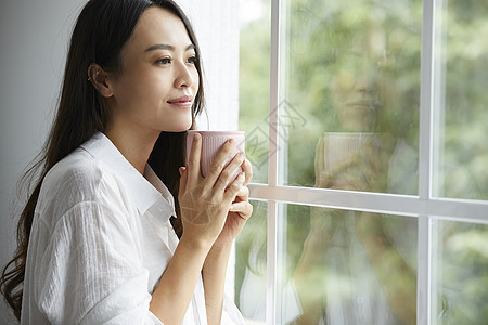 捧着水杯看向窗外的年轻女子图片