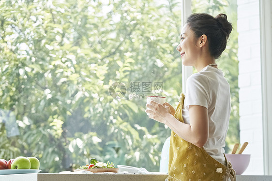 拿着水杯看向窗外的年轻女子图片