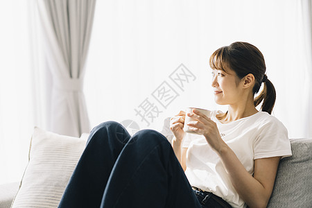 坐在沙发上喝水的女士图片