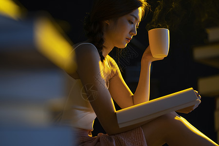 咖啡心情昏黄的灯光下年轻女人在看书阅读背景